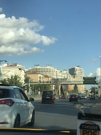 Cars on road by buildings against sky in city