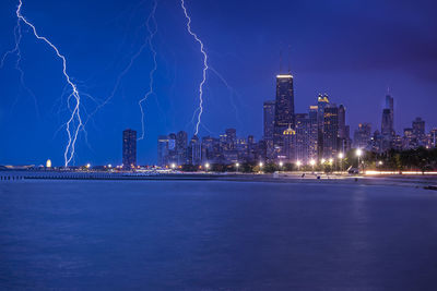 Forked lightning over city by river against sky at night