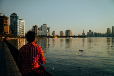 Rear view of man looking at city buildings against clear sky