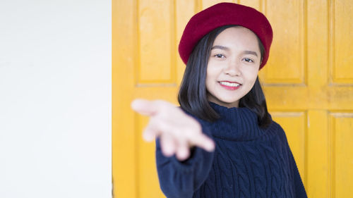 Portrait of smiling young woman standing against yellow wall