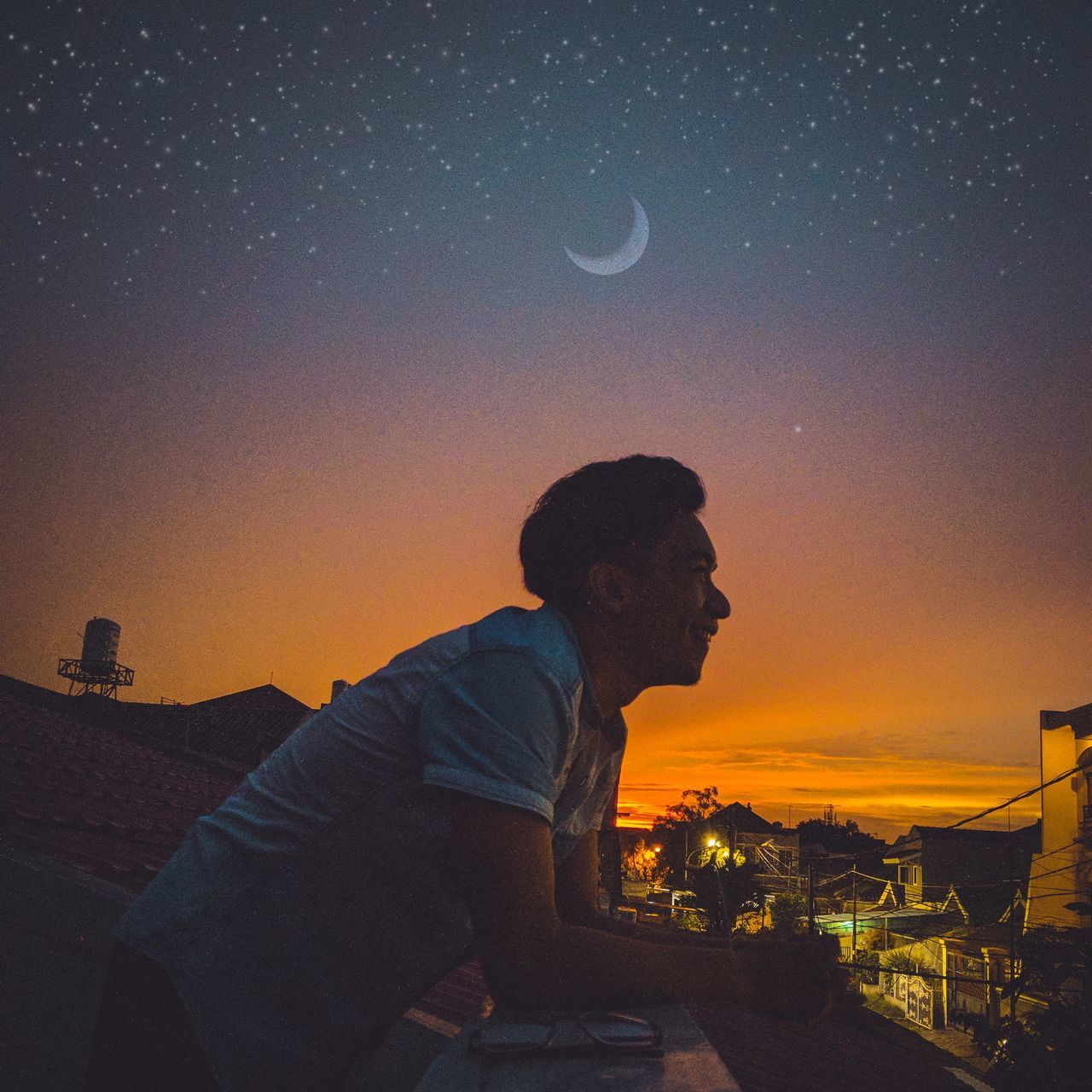 YOUNG MAN SITTING AGAINST SKY AT NIGHT