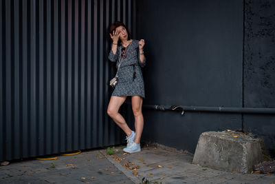 Lonely young woman in short dress stands against the wall