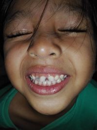 Close-up of girl with eyes closed showing teeth in darkroom
