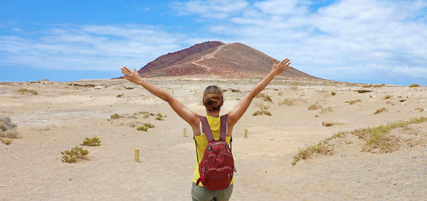 Rear view of woman with arms raised standing at desert