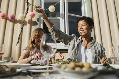 Happy young man enjoying food with friend during dinner party at cafe