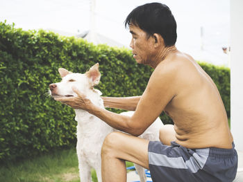 Side view of shirtless man touching dog in back yard