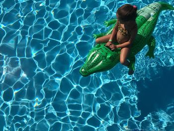 High angle view of girl sitting on inflatable crocodile in swimming pool