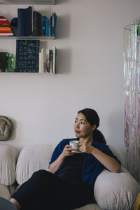 Thoughtful woman with coffee cup sitting on sofa at home