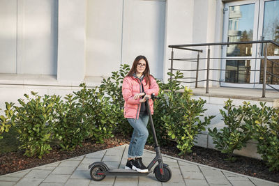 Millennial young girl in a pink jacket on an electric scooter