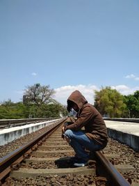 Side view of man sitting on railroad track against sky