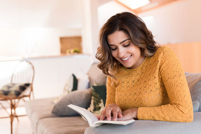 Young smiling woman reading book while sitting at home