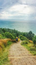 Footpath by sea against cloudy sky