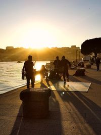 Silhouette people on sidewalk in city against sky during sunset