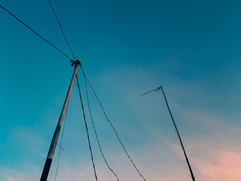 Low angle view of silhouette electricity pylon against blue sky