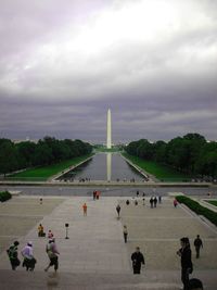 Tourists in front of building against cloudy sky