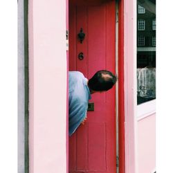 Rear view of man peeking through open red door