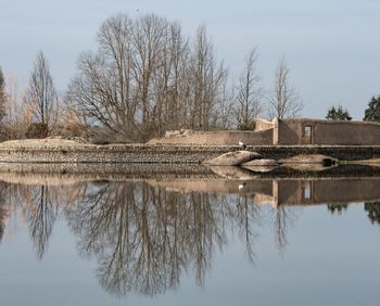 Reflection of bare trees in lake against sky