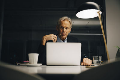 Dedicated senior male entrepreneur looking at laptop while working late in creative workplace