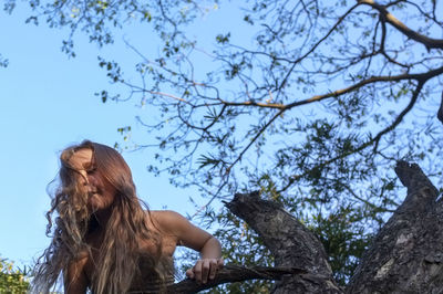 Low angle view of woman sitting on tree against sky