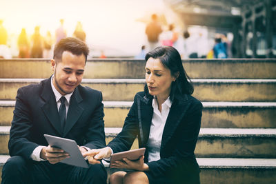 Business people discussing over digital tablet while sitting on steps