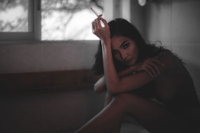 Portrait of young woman with cigarette sitting in bathroom at home