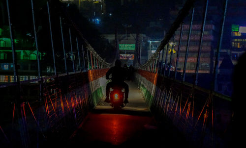 Rear view of man standing on illuminated bridge at night