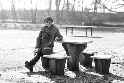 Young woman sitting on seat at park during winter