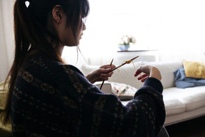 Young woman knitting wood with needle in living room