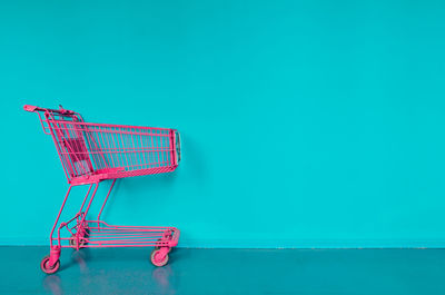 Red shopping cart on floor against blue wall