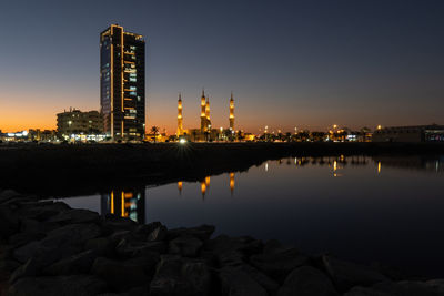 Illuminated buildings by river against sky at night