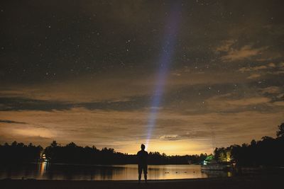 Young man painting with light by lake against starry sky