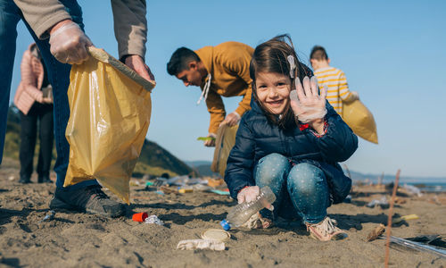 Portrait of cute girl gesturing while picking garbage at beach