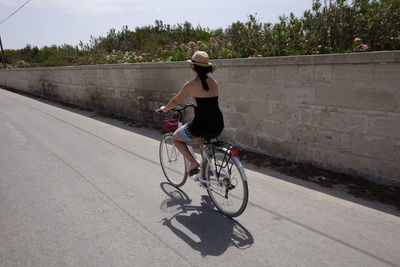 Rear view of woman cycling on road during summer