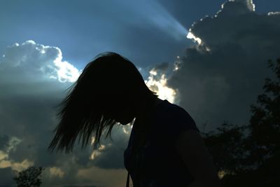 Side view of silhouette woman tossing hair while standing against sky