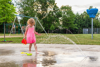  small beautiful girl in pink dress having fun at fountain playground in park