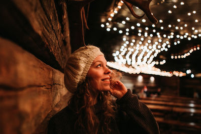 Smiling young woman looking at illuminated decorative lights during night