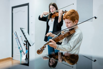 Female teacher and boy playing violins during lesson in modern music school