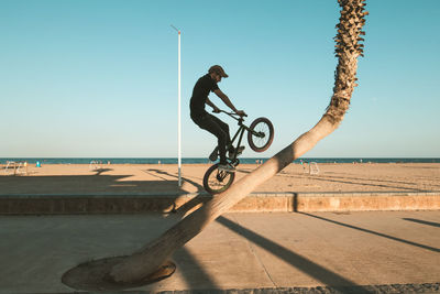 Man riding bicycle by sea against clear sky