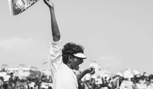 Young man holding flag while shouting at rally with crowd in background