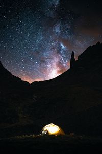 Illuminated tent by mountains against milky way at night