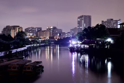 Illuminated buildings by river against sky in city at night