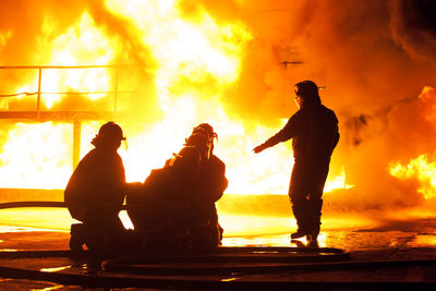 Silhouette firefighters spraying water on fire at night