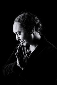 Mature woman praying while standing against black background