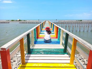 Rear view of woman sitting on pier against sky