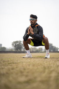 Young indian sports man doing squats in the field. sports and healthy lifestyle concept.