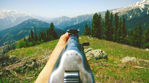 Rear view from gunpoint of man sitting on mountain against sky