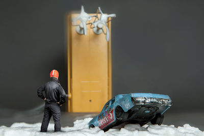 Tilt-shift image of man standing on snow covered field with electric mixer and toy car