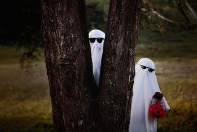 Men wearing halloween costumes hiding behind tree in forest