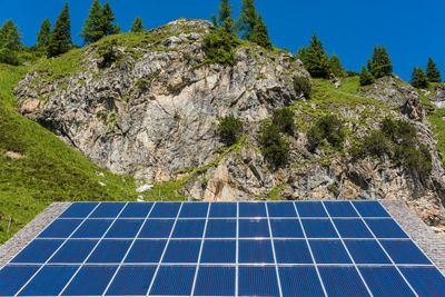 Solar photovoltaic panels against the backdrop of rocky mountains covered with green plants trees