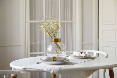 Served white table with ceramic plates and gypsophila flowers in glass vase